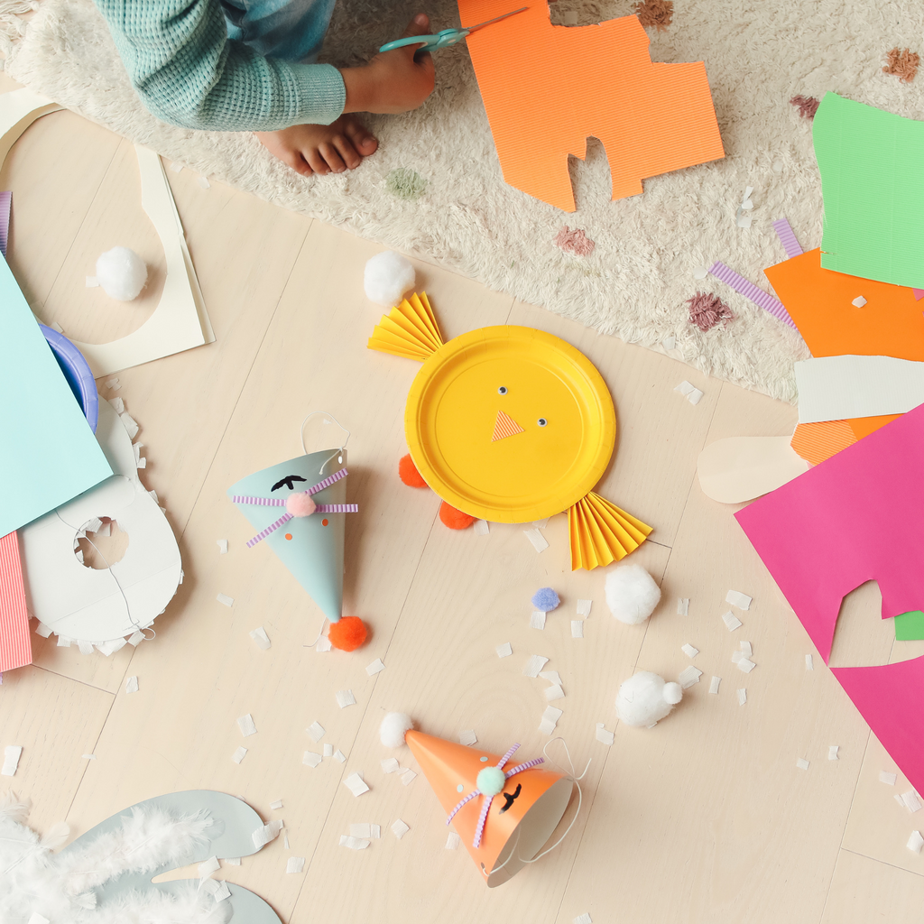 colourful craft supplies spread over a beige floor with a child cutting cardboard.