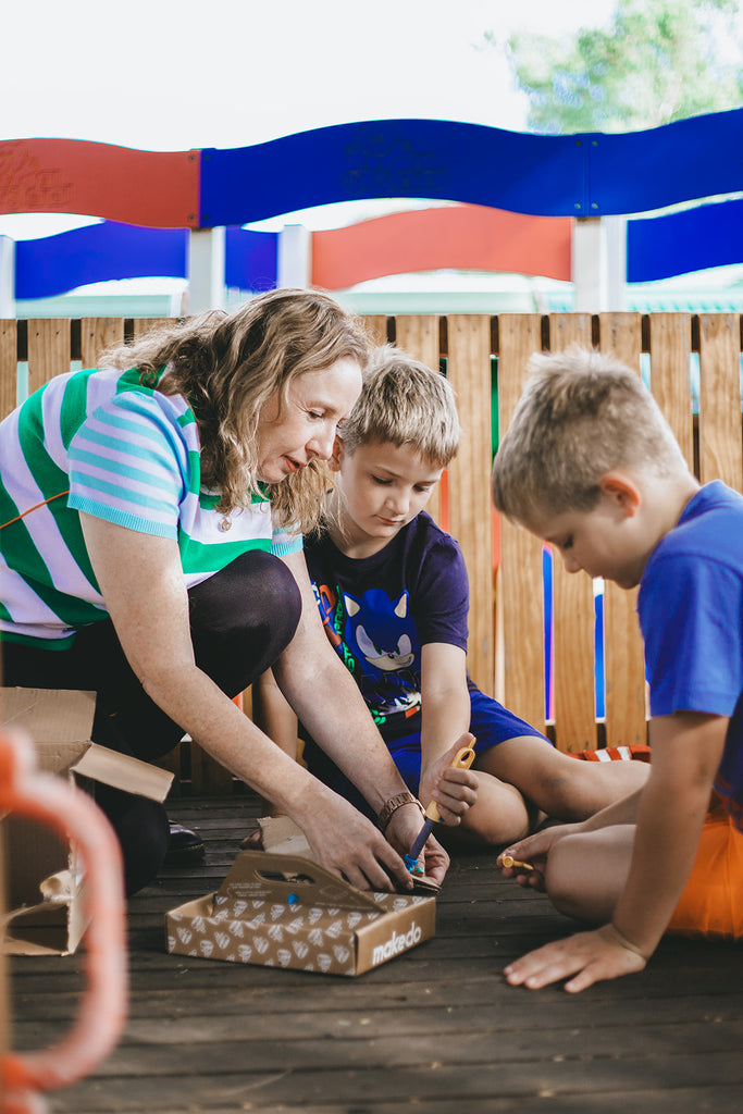 Image shows Kylie Toynton and two primary school aged boys playing outside with the Makedo cardboard building kit, part of the Curious Kids Play Box for At-home therapy