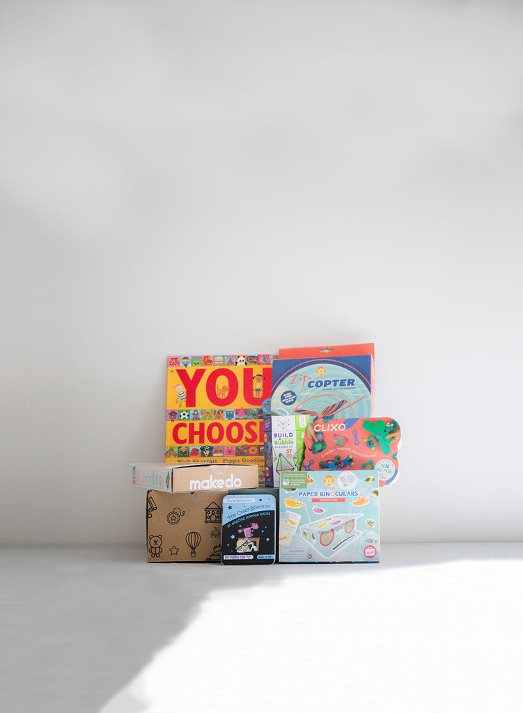 Image displays products featured in the Curious Kids  at-home therapy box focusing on attention, thinking and planning skills. Images shows, books, games, emotions visuals, STEM tools and therapy guide.
